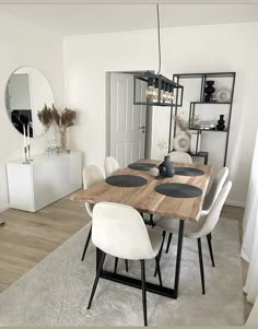 a dining room table with white chairs and a mirror on the wall in front of it