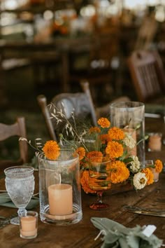 an arrangement of flowers and candles on a wooden table in a restaurant or dining room