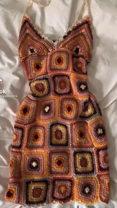 a crocheted dress sitting on top of a white bed next to a pillow