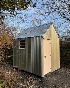 a small metal shed sitting on top of a gravel field next to trees and bushes