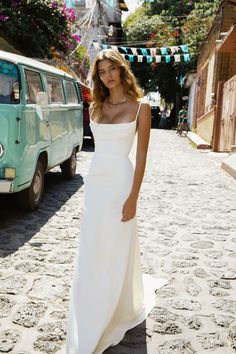 a woman in a white dress standing on a cobblestone street with an old vw van behind her