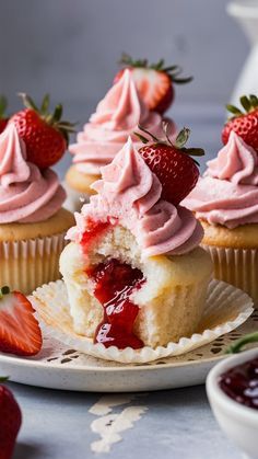 strawberry cupcakes with pink frosting and strawberries on the plate next to them