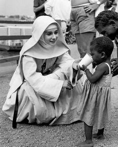 a black and white photo of a woman in a nun outfit feeding a small child