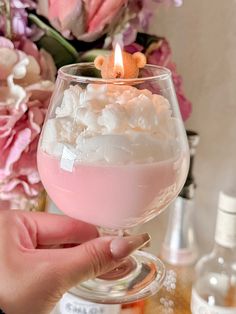 a person holding a wine glass filled with pink liquid and marshmallows in it