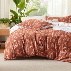 a bed with an orange and white comforter on top of it next to a potted plant