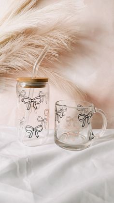 two glass mugs sitting next to each other on a white sheet with feathers in the background