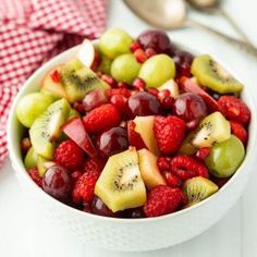 a white bowl filled with fruit on top of a table next to a fork and spoon