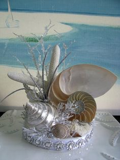 an arrangement of seashells and seaweed in a silver basket on a table