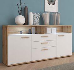 a white and wood sideboard in a living room with blue walls, vases and pictures on the wall