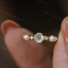 a woman's hand holding a gold ring with white stones