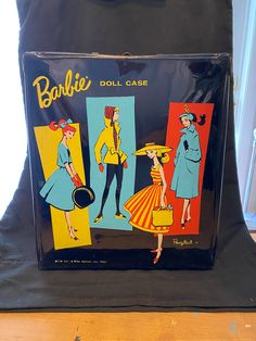 an old fashioned barbie doll case sitting on top of a wooden table next to a black bag