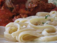 some noodles and meat on a white plate with red sauce in the backround