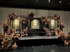 a stage set up for a wedding with flowers and candles on the floor, surrounded by curtains