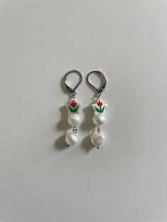 two pairs of earrings with flowers and pearls hanging from hooks on a white table top