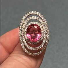 a person holding a ring with a pink stone in it's center and surrounded by white diamonds