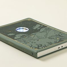 a green book with an oval hole in the middle on a white surface, next to a computer mouse