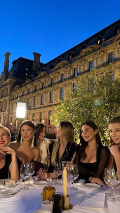 a group of women sitting at a dinner table in front of an old building with wine glasses on it