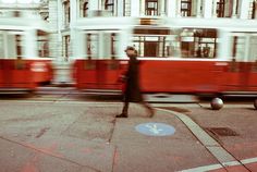 a person walking across a street next to a red and white train