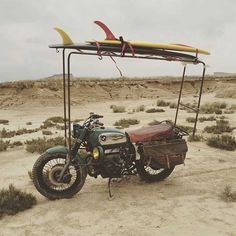 a motorcycle parked in the desert with a surfboard on top