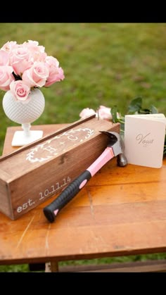 pink roses in a vase on top of a wooden table next to a small box