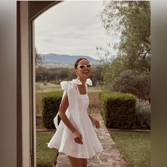 a woman wearing sunglasses and a white dress is standing in front of an open door