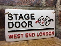 a sign that says stage door west end london with two faces on the front and back