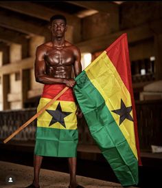 a man standing next to a flag holding a wooden stick in one hand and a pole in the other