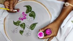 two hands are drawing flowers on a white plate with pink candles in front of them