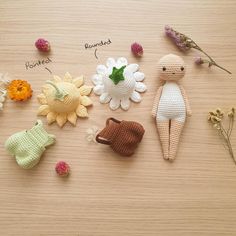 several crocheted dolls are arranged on a wooden surface with flowers and leaves around them