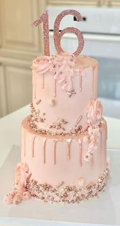 a pink birthday cake decorated with flowers and icing is displayed on a white table