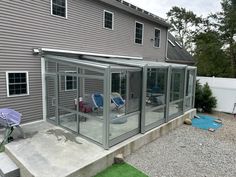 an enclosed patio with chairs and umbrellas in the back yard, next to a house