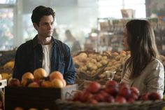 a man standing next to a woman in front of a produce stand filled with fruit