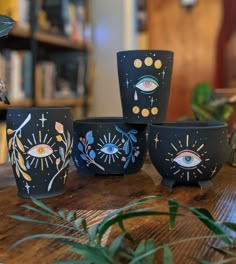 five black bowls with designs on them sitting on top of a wooden table next to plants