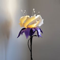 a white and purple flower is sitting on a black stand with its light turned on