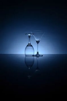 two martini glasses sitting next to each other in front of a blue background with reflections