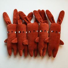 five red stuffed animals lined up in a row on a white surface with eyes and ears