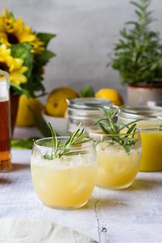 two glasses filled with lemonade and rosemary garnish on a table next to flowers