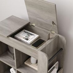 an open book shelf with magazines and a cell phone on it, next to a white wall