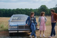 three people standing next to a car in a field