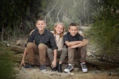 three children are sitting on a log in the woods and posing for a family photo