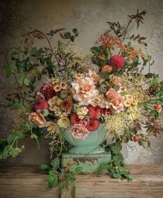 a vase filled with lots of flowers sitting on top of a wooden table next to a wall