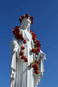 the statue is adorned with red roses and greenery on it's head, in front of a clear blue sky