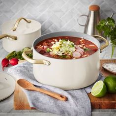 a large pot filled with soup on top of a wooden cutting board next to limes