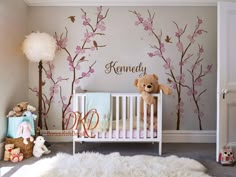 a baby's room with a teddy bear in the crib and cherry blossom trees painted on the wall