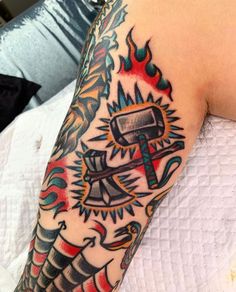 an arm with some tattoos on it and a hammer in the middle, surrounded by flames