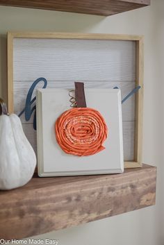 a white pumpkin sitting on top of a wooden shelf next to a framed piece of paper