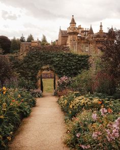 an old castle with lots of flowers in the foreground and a pathway leading to it