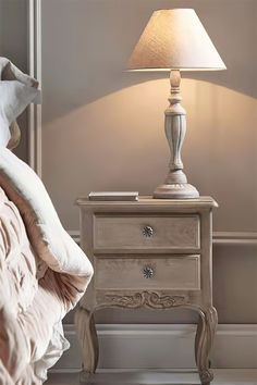 a white nightstand with a lamp on it next to a bed