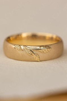 a gold wedding band with leaves on the side and a plain surface in the background