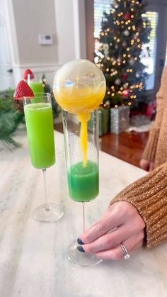 a woman is holding two glasses with different colored drinks in them on a counter top